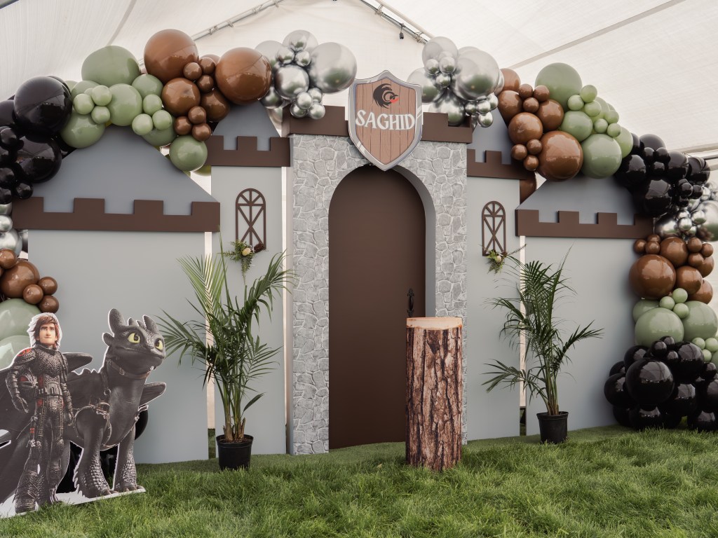 How to Train Your Dragon themed party setup with custom castle backdrop, luxe balloon garland in earthy tones, greenery accents, and character cutouts — full-service event design and rentals in Denver, Colorado.