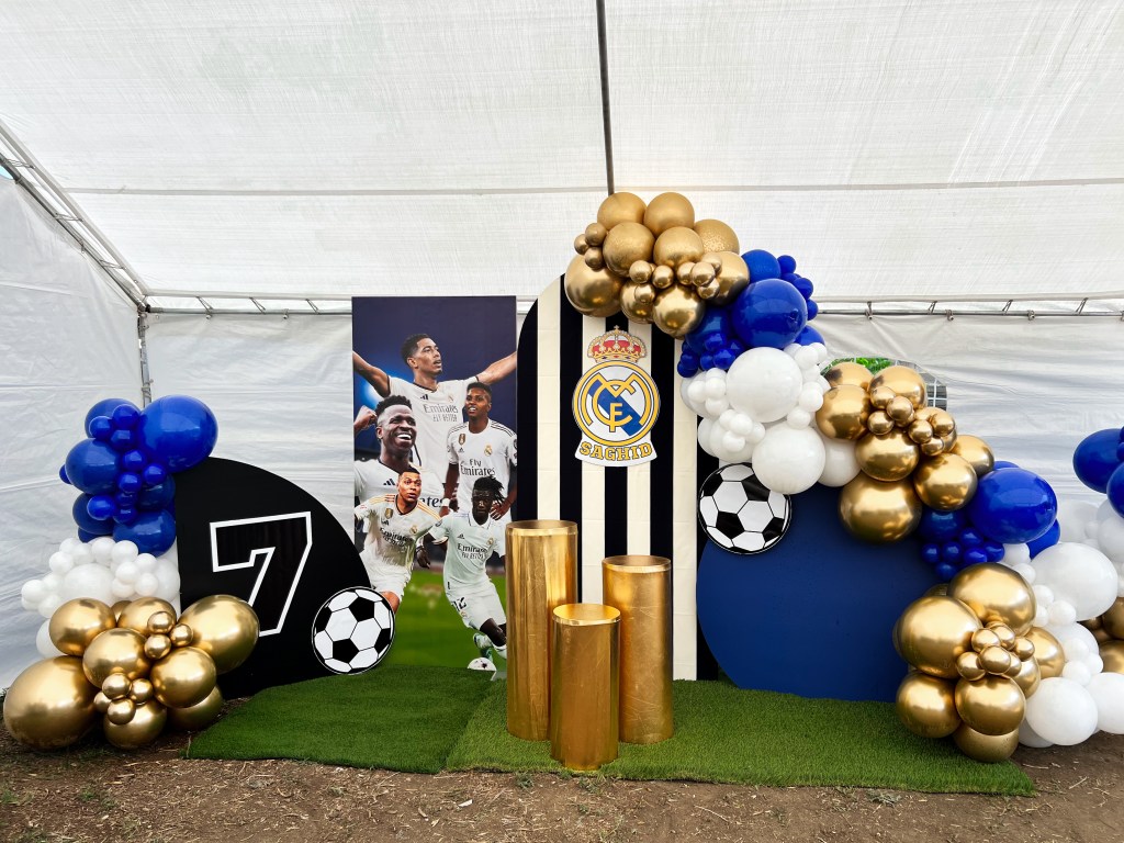 Chuchi's Events Real Madrid-themed setup showcasing a custom-designed backdrop with a stunning blue, gold, and white balloon garland. This vibrant decor features elegant dessert pedestals and personalized signage, perfect for soccer-themed birthday parties, celebrations, or game day events in Denver.