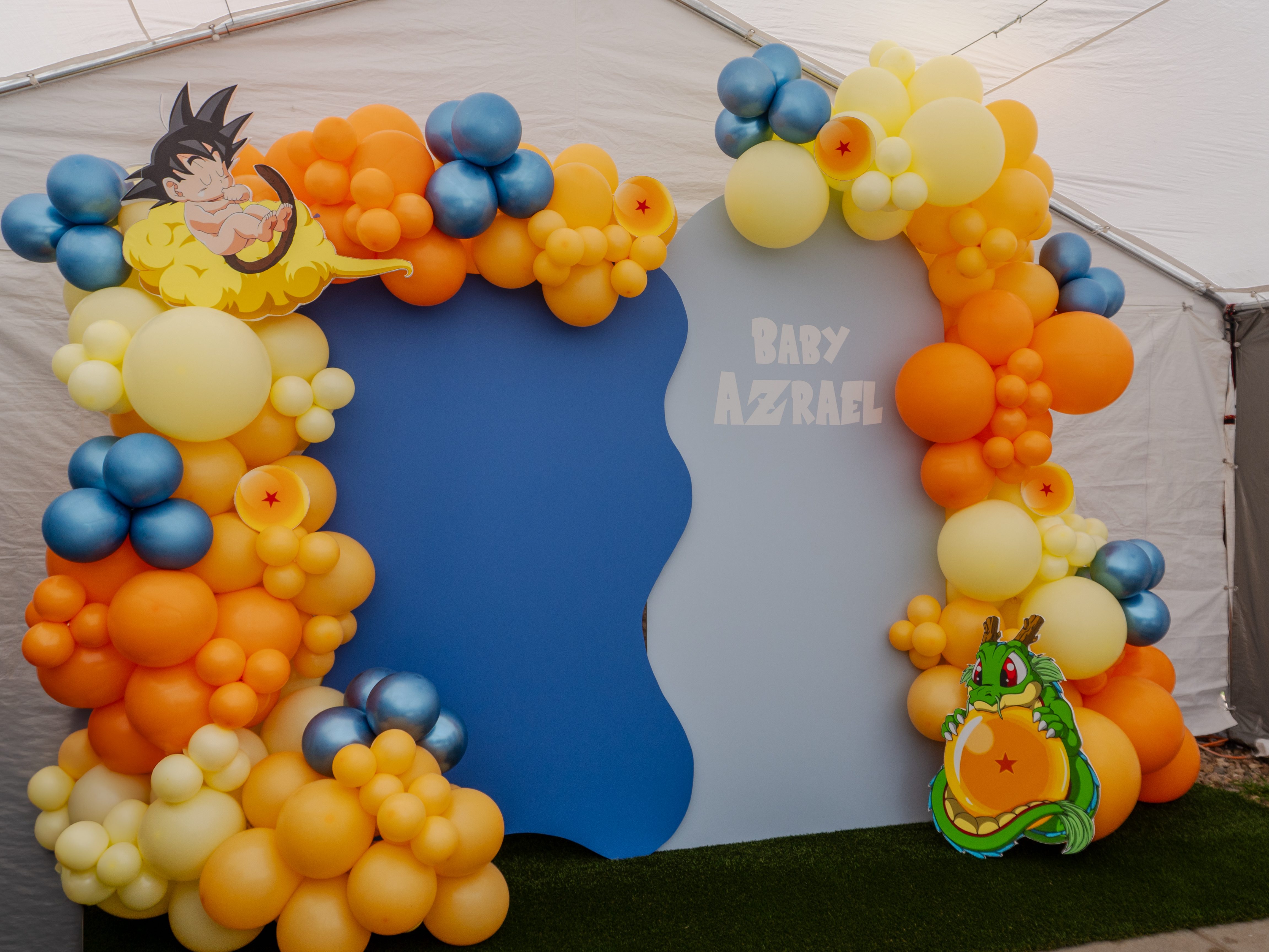 Dragon Ball-themed baby shower setup featuring Chuchi’s Events wavy wall backdrop rental with vibrant orange, yellow, and blue balloon garland, Baby Goku and Shenron cutouts, perfect for parties and events in Denver.