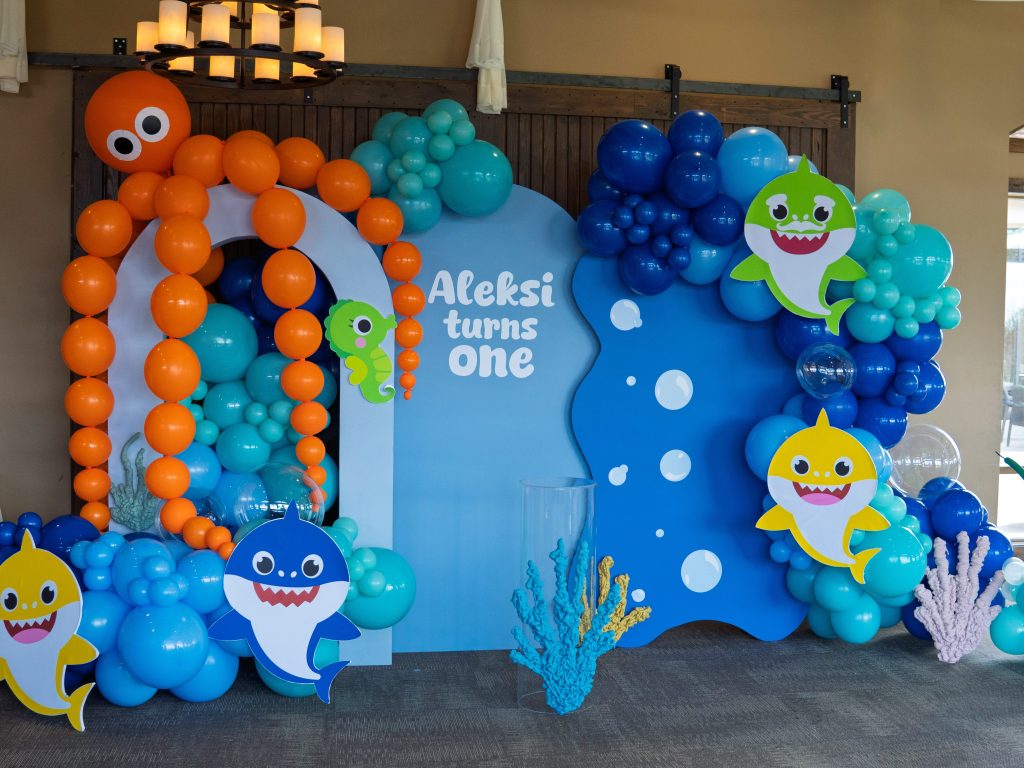 Ocean-themed first birthday party setup by Chuchi's Events, a Denver-based party rental and balloon decor company. Features custom balloon garlands and arches, sea creature props, Baby Shark cutouts, and layered backdrop rentals. Full-service installation includes luxury balloon styling, themed props, and event setup—perfect for kids' parties and milestone celebrations in the Denver metro area