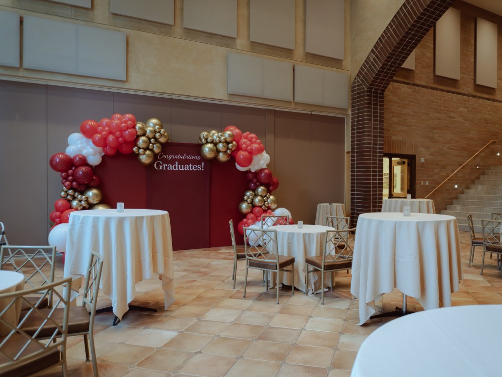 Balloon backdrop setup for University of Denver corporate event featuring deep red and gold balloons with custom vinyl on a burgundy backdrop.